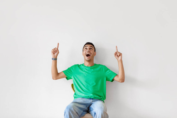 Excited arab man pointing and looking up at copy space, opening mouth in shock on light studio wall background, free space. Guy showing place for your text or design - Photo, Image