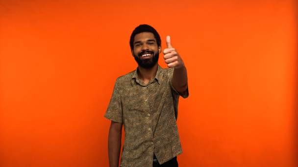 alegre afroamericano hombre con barba mostrando el pulgar hacia arriba sobre fondo naranja - Foto, Imagen