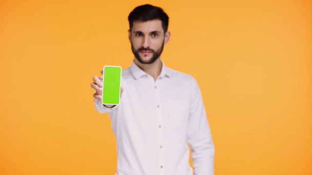 bärtiger Mann im weißen Hemd hält Smartphone mit grünem Bildschirm isoliert auf gelb - Foto, Bild