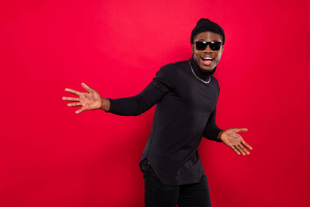 Portrait of attractive cheerful funky guy wearing black look having fun moving isolated over bright red color background. - Foto, Imagen
