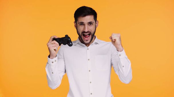 KYIV, UKRAINE - NOVEMBER 21, 2019: excited man in shirt holding joystick and rejoicing isolated on yellow - Fotoğraf, Görsel