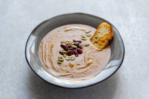 Healthy vegan pumpkin soup with red beans, pumpkin seeds, coconut cream and slices of fried bread - Photo, Image