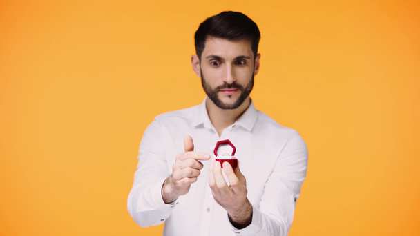 bearded man in white shirt pointing at box with engagement ring while making proposal isolated on yellow - Photo, image