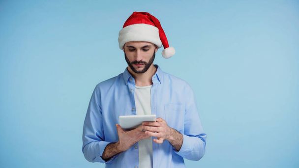 bearded man in red santa hat using digital tablet isolated on blue  - Photo, Image
