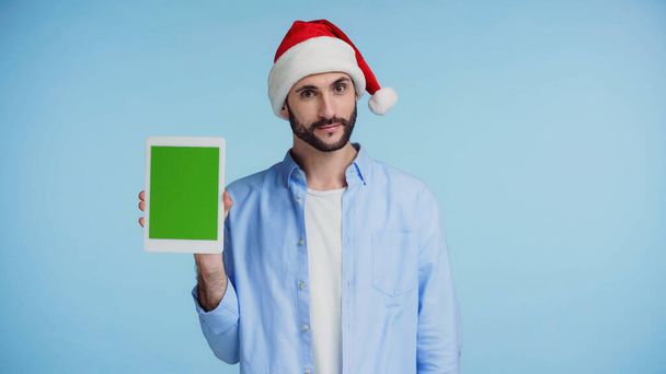 man met baard in rode kerstman hoed met digitale tablet met groen scherm geïsoleerd op blauw  - Foto, afbeelding