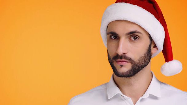 portrait of bearded man in red santa hat looking at camera isolated on yellow - Photo, Image