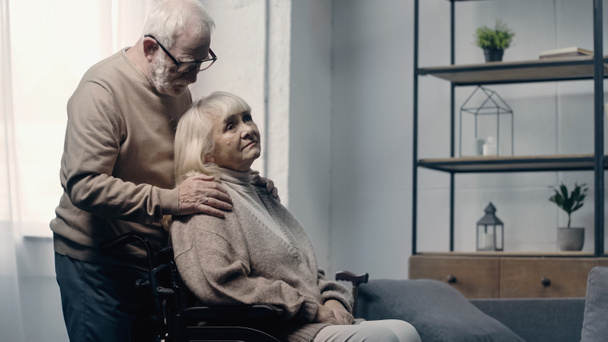 Vanhempi mies, joka rauhoittaa vammaista vaimoaan pyörätuolissa olevalla dementialla  - Valokuva, kuva
