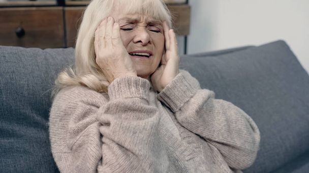 Seniorin mit Demenz hat Kopfschmerzen beim Sitzen auf Sofa - Foto, Bild