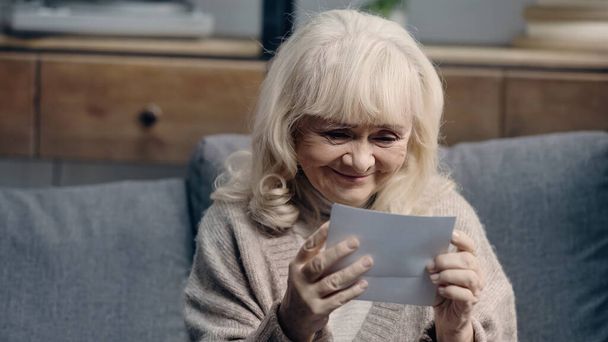 Fröhliche Seniorin mit Demenz schaut sich zu Hause gedruckte Fotos an - Foto, Bild