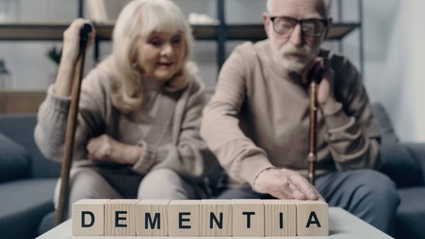 Senior woman sitting near man putting wooden cube with lettering and creating word dementia  - Photo, Image