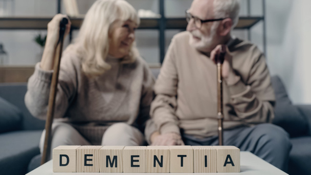 高齢者のカップルの近くのテーブルに認知症の文字が書かれた木製の立方体   - 写真・画像