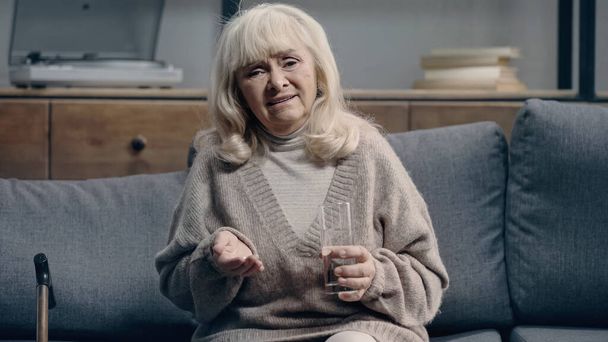 Traurige Seniorin mit Demenz hält Tabletten in der Hand und blickt in die Kamera - Foto, Bild