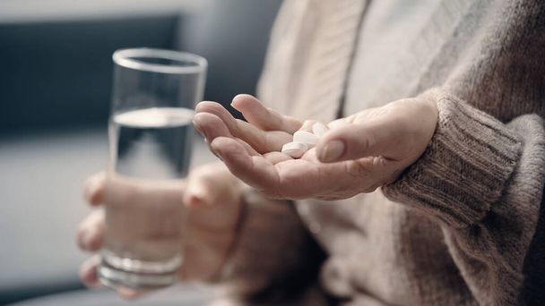 visão parcial da mulher idosa com demência segurando pílulas e vidro de água  - Foto, Imagem