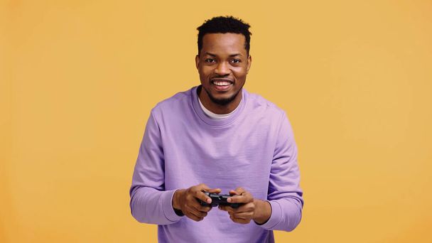 KYIV, UKRAINE - 22, 2019: Sarı üzerinde izole edilmiş video oyunu oynayan neşeli Afrikalı Amerikalı adam  - Fotoğraf, Görsel