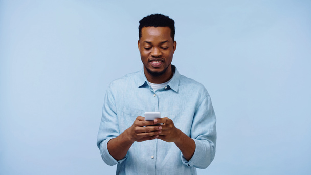 szczęśliwy Afrykanin amerykański człowiek w koszuli trzyma telefon komórkowy odizolowany na niebiesko - Zdjęcie, obraz