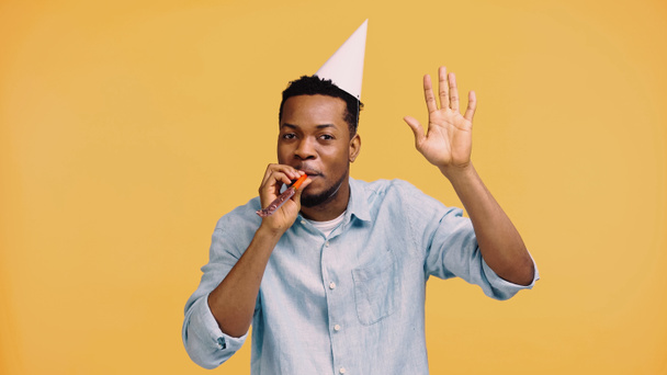 afro-américain en chapeau de fête soufflant corne et geste isolé sur jaune  - Photo, image