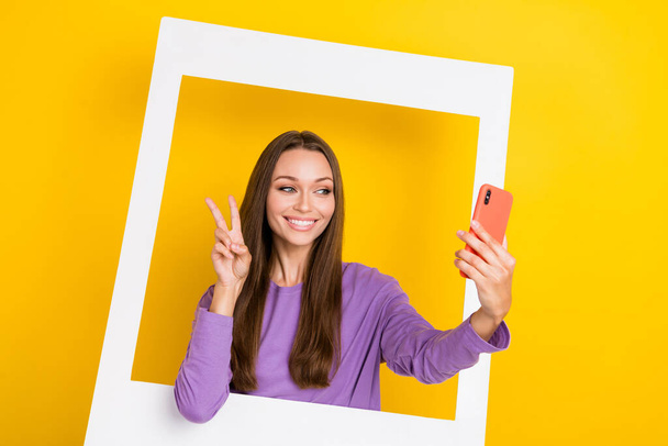Photo of positive pretty blogger stand inside white image make self portrait picture snapshot v-sign isolated on yellow color background. - 写真・画像