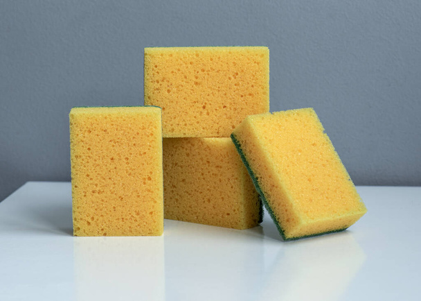 Yellow kitchen sponges on a white table. Sponges for washing dishes and other household needs. Scrub yellow sponge design, closeup Cleaning sponges. High quality photo - Photo, Image