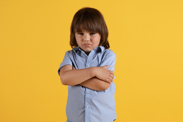 Діти ображаються. Студійний портрет милого засмученого маленького хлопчика, який ображається, стоїть зі складеними руками і плаче, позує над помаранчевим тлом
 - Фото, зображення