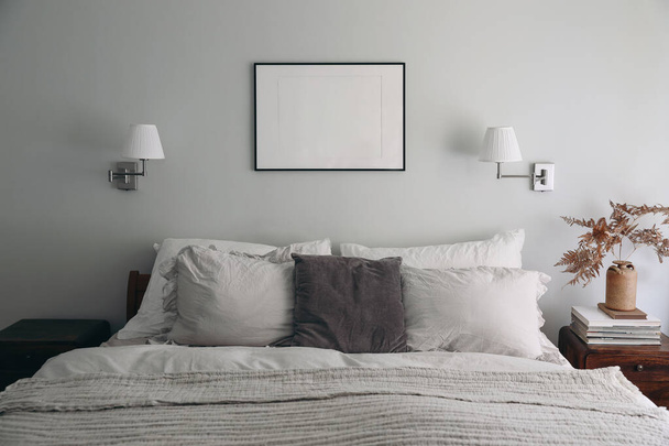 Landscape black picture frame mockup on sage green wall. Elegant bedroom view. White and grey linen pillows, blanket.Night stand with ceramic vase, dry fern and books, Scandinavian interior. - 写真・画像