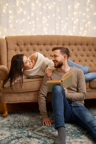 Krásný mladý milující pár sblížení mezi sebou a usmívat se, zatímco žena drží knihu. Trávit příjemné chvíle doma - Fotografie, Obrázek