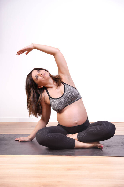 30er-40er Jahre reife schwangere Erwachsene in Sportkleidung, die sich zu Hause auf einer Yogamatte dehnt - Foto, Bild