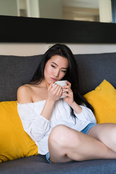 Young chinese and attractive girl having breakfast with a cup of coffee at her modern house - Foto, Imagem