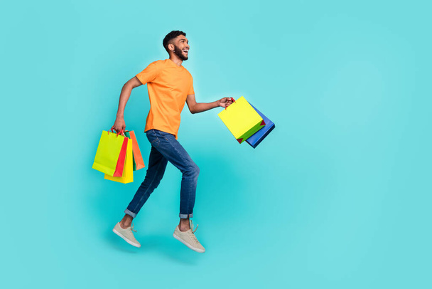 Full length profile photo of energetic guy hold packages jump run hurry empty space isolated on teal color background. - Foto, Imagem