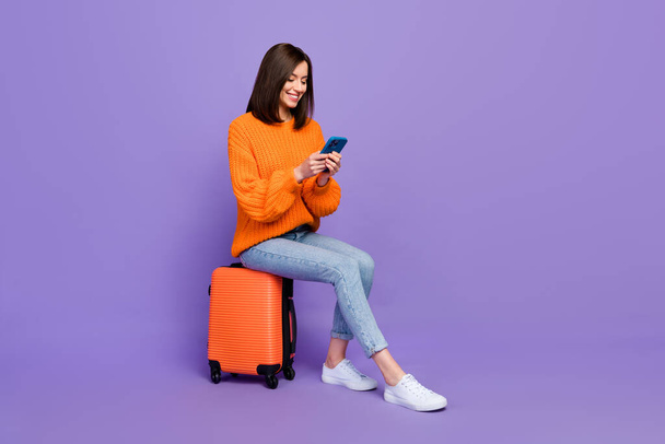 Full body photo of nice young lady typing chatting hold gadget travel wear trendy orange knitwear look isolated on violet color background. - 写真・画像