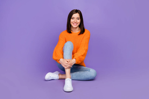 Full body photo of pretty young girl sit floor model shopping promo wear trendy orange knitwear look isolated on violet color background. - Foto, afbeelding