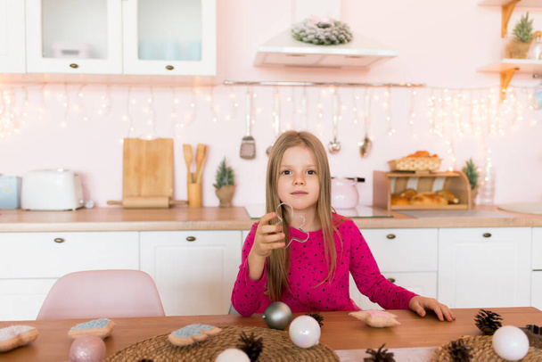 Little cheerful girl with a mold for gingerbread in the kitchen. New Year's interior in the kitchen. - Foto, Imagen
