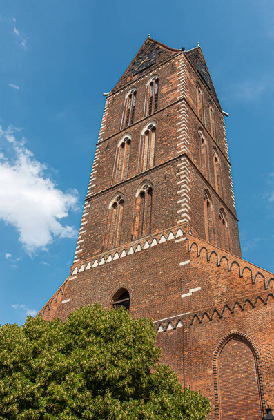 Германия, Висмар - 13 июля 2022 года: Задняя часть St. Marienkirchturm, церковь Св. Марии башня, поврежден во время Второй мировой войны, как памятник под голубым облачным ландшафтом, красный кирпич потемнел, зеленая листва - Фото, изображение