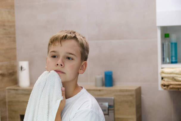 Tükröződik, ahogy egy iskolás törülközővel törli az arcát, miután kimosta a fürdőszobát. Reggeli higiéniai eljárások. - Fotó, kép