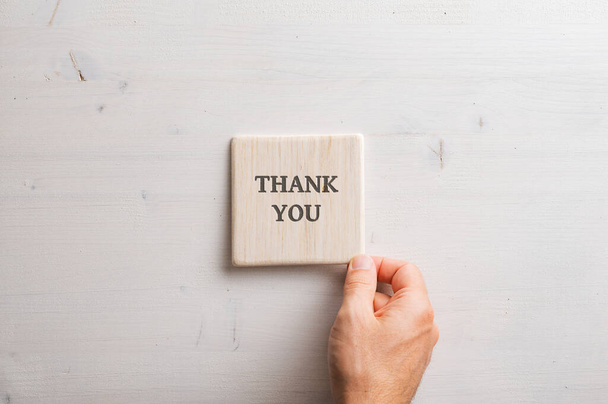 Male hand placing a wooden tile with a Thank you sign on it over a simple plain wooden background. - Photo, Image