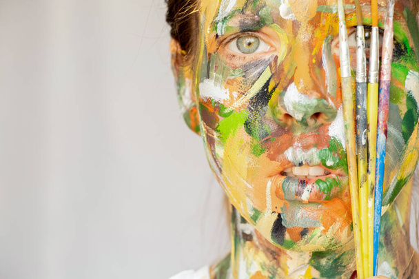 La cara de una niña pintada con acuarelas de diferentes colores y pinceles sobre un fondo aislado, creatividad, pintura en la cara - Foto, Imagen