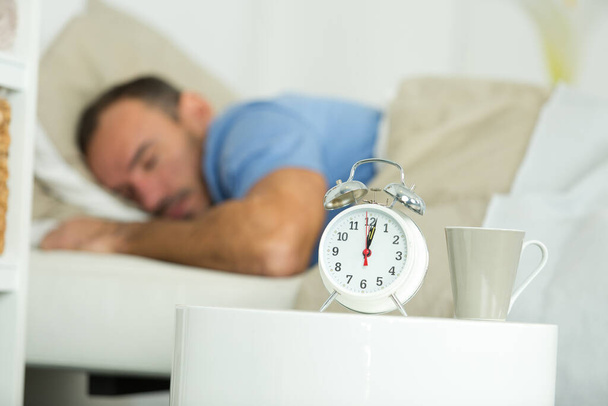 man asleep in bed alarm clock showing twelve oclock - Fotografie, Obrázek