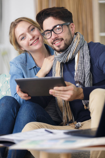 Feliz pareja joven con la tableta tumbada en el sofá en casa
 - Foto, Imagen