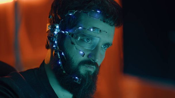 Ragazzo bruna lavora al computer con luci al neon in background. Cyberpunk. Indossare un futuristico occhiali con un occhio solo e microfono. Sfondi informatici e di fantascienza. - Foto, immagini
