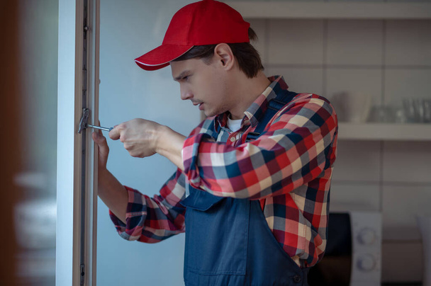 Retrato de cintura hacia arriba de un reparador atornillando la cerradura en el marco de la ventana con un destornillador - Foto, imagen