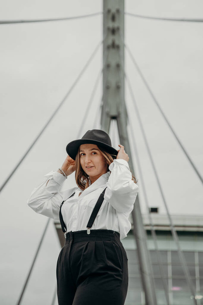 Elegant fashionable woman wearing white shirt, black hat. Confident girl posing black suit and hat. Business girl in suit. - Фото, зображення
