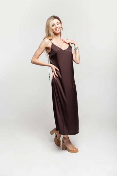 Fashion happy pretty woman blonde model in stylish vintage brown strappy dress with shoes on a white background - 写真・画像