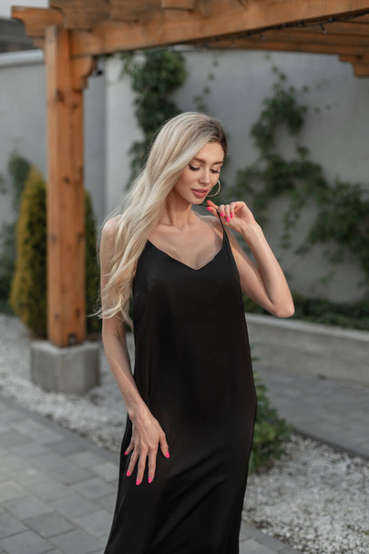 jolie femme blonde mignonne à la mode dans élégant élégant noir robe longue promenades dans la ville en plein air - Photo, image