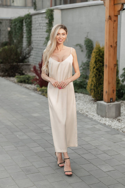 Happy fashion mooi meisje met glimlach in stijlvolle elegantie beige sexy strappy jurk met schoenen wandelingen op straat - Foto, afbeelding