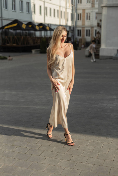 Moda mujer bastante elegancia modelo rubio en elegante vestido largo vintage beige con zapatos camina en la calle al atardecer luz - Foto, imagen