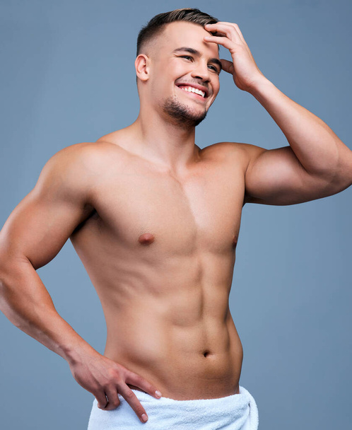 Muskeln mit einem Hauch von Scheu. Studioaufnahme eines muskulösen jungen Mannes, der mit einem Handtuch vor grauem Hintergrund posiert - Foto, Bild