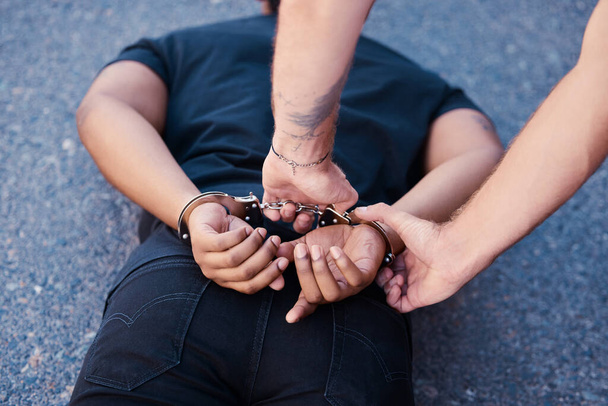 Crime arrest, scam and criminal man with security officer handcuffs on the ground. Back hands of legal justice on a road of a caught guy in the act going to court, jail or prison with police officer. - Фото, изображение