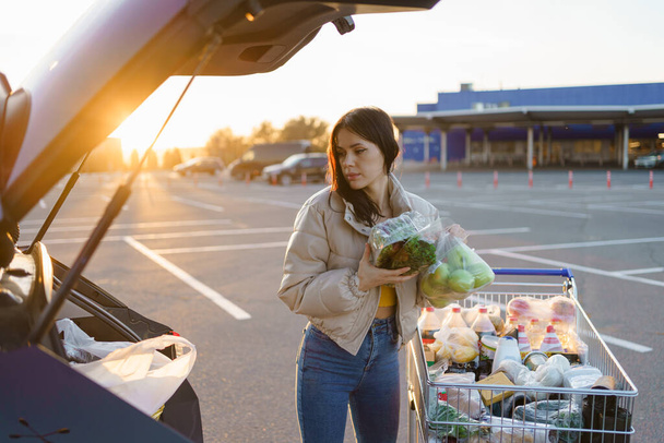 Frau nach dem Einkauf in einem Einkaufszentrum oder Einkaufszentrum. Schöne junge Frau, die in einem Supermarkt einkauft und die Einkäufe auf dem Parkplatz in ihr Auto legt. Hochwertiges Foto - Foto, Bild