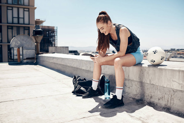 Sports, soccer and woman with phone relax after rooftop game, competition or training practice. Football exercise, workout and athlete with smartphone laugh at fitness meme or streaming comedy video. - Foto, afbeelding
