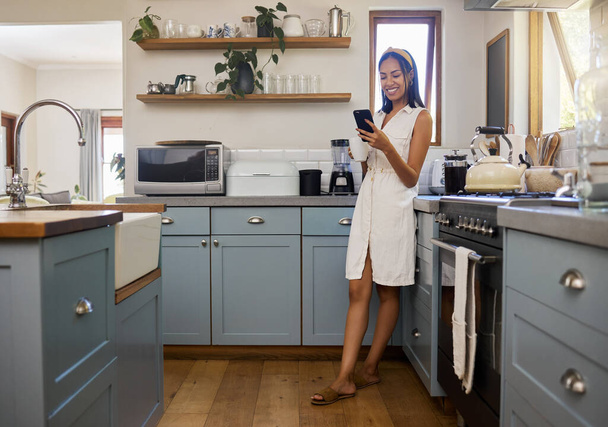 Coffee, phone and woman in kitchen on social media, text message or online app in home. Relax, tea or reading news or mobile online web surfing with happy, smile and female in Brazil on 5g smartphone. - 写真・画像