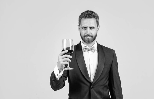 handsome tuxedo man cheers with glass of red wine hold gift box behind back, copy space, sommelier. - Photo, Image